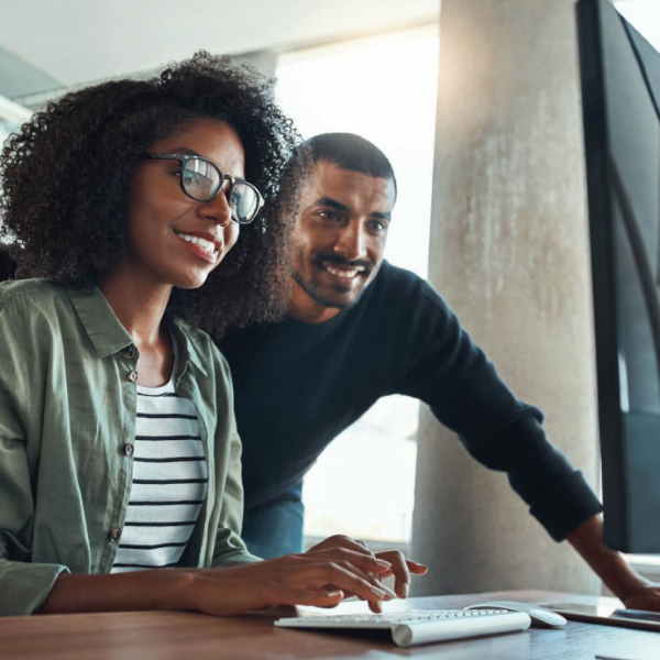 A seated woman and a standing man look and smile at a computer screen.