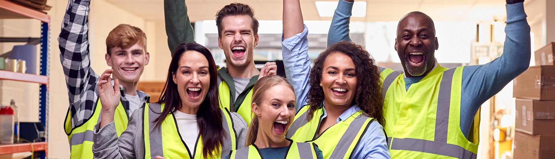 Three men and three women wearing yellow hi-viz jackets celebrate and smile at the camera.