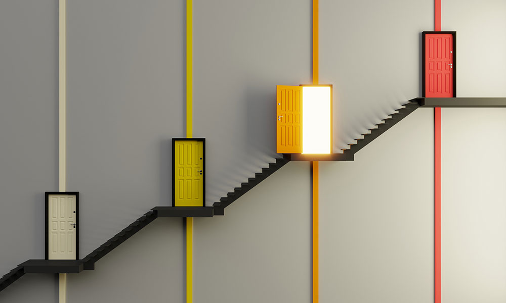 black stairway is depicted side on against a grey background. The first floor has a cream coloured door, second a yellow, third an orange, fourth a red. All are closed other than the third orange door which is open and has light shining from within.