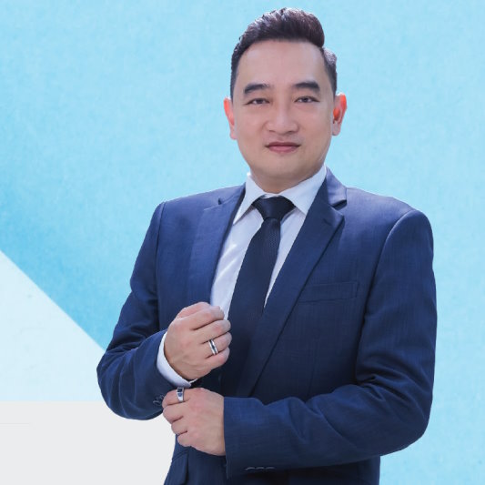 Procurri employee Leonard Chong stands facing the camera in a suit against a blue and white background.